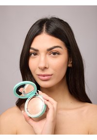 Kompaktpuder in einer mintgrünen Verpackung mit Spiegel, mit einem glatten, hellen Puder im Inneren, gehalten von einer Person mit langen Haaren.