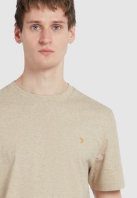 T-shirt beige chiaro realizzato in tessuto morbido. Presenta un collo rotondo e maniche corte. Piccolo logo arancione sul petto sinistro.