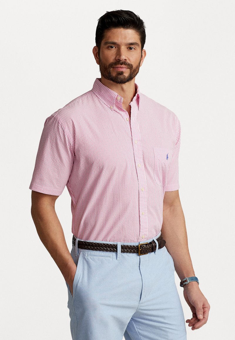 Īsām piedurknēm, pogājams krekls ar sarkaniem un baltajiem strīpām. Iespējama klasiskā apkakle, krūšu kabata un brīva piegriezuma forma. Valkāts ar gaiši ziliem biksēm.