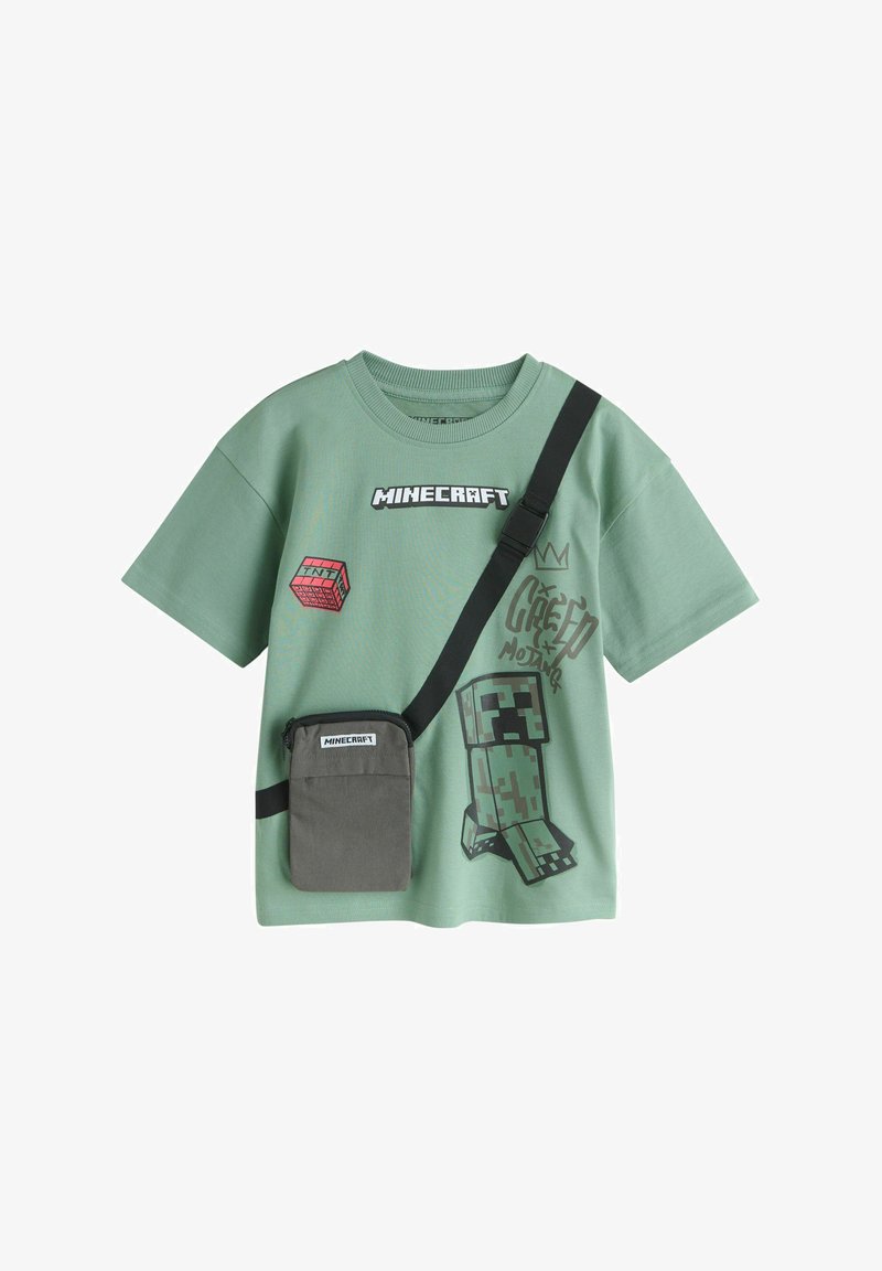 T-shirt vert à manches courtes Minecraft avec un graphisme Creeper, un bloc de TNT, et une pochette noire portée en bandoulière avec une étiquette Minecraft.