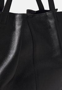 Borsa a spalla in pelle nera con superficie testurizzata, dettagli delle cuciture lisci e doppi manici. Il design è semplice e funzionale.