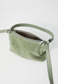 Green suede crossbody bag with a zipper closure, textured surface, and a matching strap, featuring silver hardware accents.