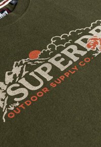 Olijfgroene sweatshirt met een gestructureerde afwerking, voorzien van een grote wit-rode grafiek met bergen en de tekst "SUPERDRY OUTDOOR SUPPLY CO."