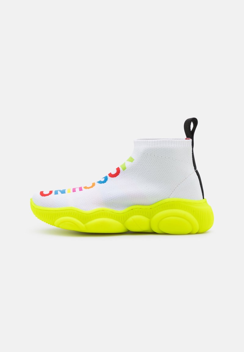 Bílé pletené slip-on tenisky s multikolórovým textem "UNINHIBITED", jasně neonově zelenou podrážkou, texturovaným povrchem a černým akcentem na patě.