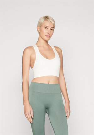 Hvit kort athletic topp med brede stropper, kombinert med høy midje, teksturerte, lysegrønne tights. Enkel design, elastisk stoff.
