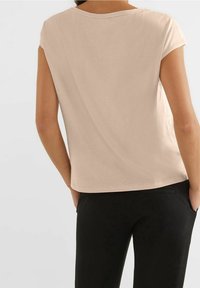 Krátký béžový rukáv s volným střihem a kulatým výstřihem. Hladký povrch, jednoduchý design a mírné splývání na zadní straně.