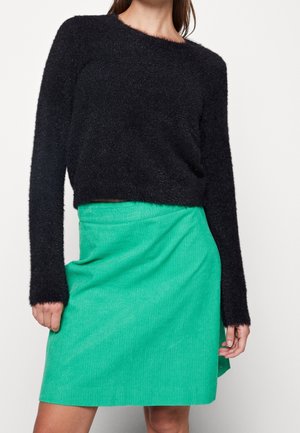 Pull noir en peluche à manches longues associé à une mini-jupe en velours côtelé verte. Le pull a un col arrondi ; la jupe présente une finition texturée.