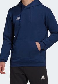 Sweat à capuche bleu marine avec une poche frontale, des cordons de serrage, et un logo Adidas blanc brodé sur la poitrine. Tissu doux, coupe décontractée.