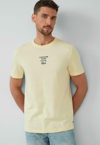 Gelbes Baumwoll-T-Shirt mit kurzen Ärmeln, auf dem die schwarze Aufschrift "LONESOME RIDER SOCIAL Club" mittig auf der Brust zu sehen ist.