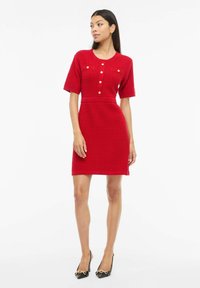 Robe rouge légère texturée avec manches courtes, encolure ronde et fermeture par boutons. Dotée de deux poches poitrine et d'une taille cintrée.