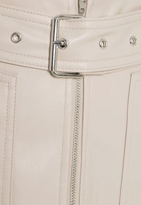 Jupe en cuir beige clair avec des accessoires argentés, comprenant une ceinture large à boucle, une fermeture éclair et des détails de couture verticale.