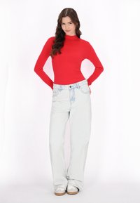 Maglione a collo alto rosso a costine abbinato a jeans larghi blu chiaro. L'outfit è completato da sneakers bianche con suola beige.