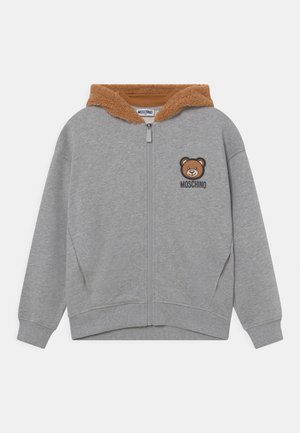 Graue Zip-Hoodie mit braunem Kunstfellfutter in der Kapuze. Mit einem braunen Bärenmotiv und dem "MOSCHINO"-Logo auf der linken Brust. Rippbündchen an den Ärmeln und am Saum.
