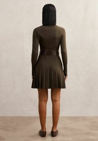 Olíva zöld kötött ruha hosszú ujjakkal, testhez simuló felső résszel és pliszírozott szoknyával. Széles barna övvel kiegészítve a deréknál.