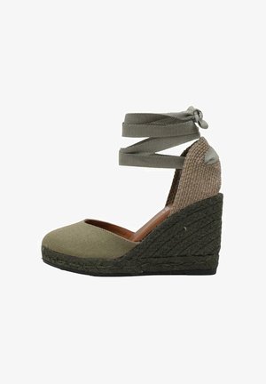 Espadrille à semelle compensée avec tige en toile vert olive, talon en jute tissé et détail de lien à la cheville. Bout arrondi et panneau latéral texturé.