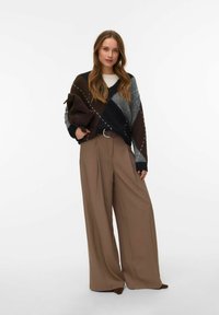 Pulover z V-izrezom z diamantnim vzorcem v rjavi, sivi in črni barvi. Kombiniran z visokim pasom in širokimi bež hlačami.