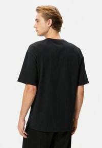 Musta puuvillainen t-paita rentoa mitoitusta, jossa on lyhyet hihat, klassinen pyöreä pääntie ja yksinkertainen selkäosa ilman koristeluja.