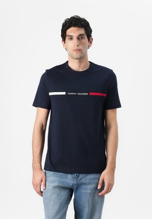 Navy cotton t-shirt with short sleeves, crew neck, featuring a white and red horizontal stripe with "TOMMY HILFIGER" text across the chest.