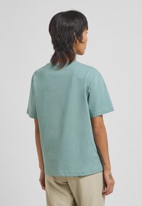 Korte mouwen T-shirt in licht teal, gemaakt van katoen. Ronde hals, relaxte pasvorm, zachte textuur en gestikte details aan de onderkant.