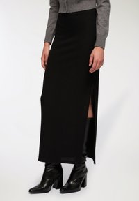 Gonna maxi nera a costine con spacco laterale, abbinata a stivaletti neri con tacco. Il materiale sembra strutturato e aderente in vita.