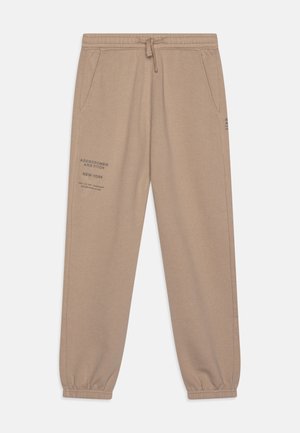 Beige joggingbukser lavet af en bomuldsblanding. Har elastiske mansjetter, sidelommer og trykt branding på venstre lår.