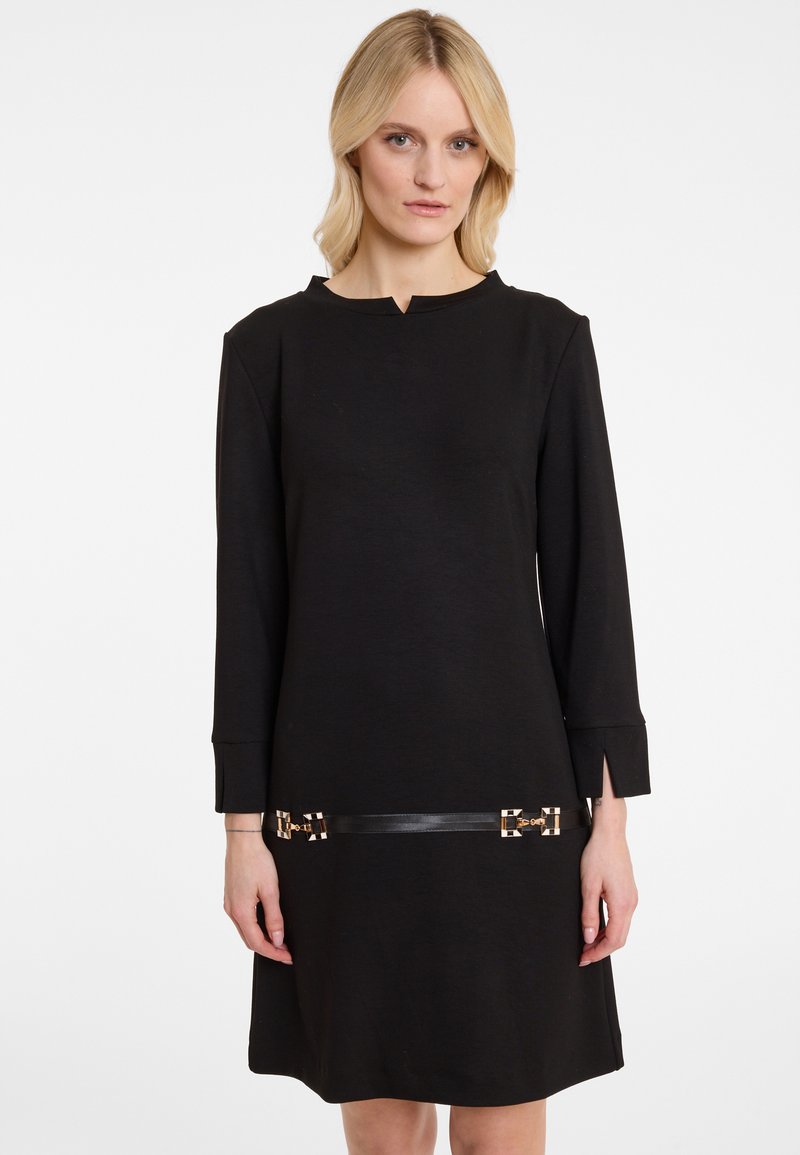 Schwarzes langärmliges Kleid mit Rundhalsausschnitt, ausgestattet mit goldenen Hardware-Details und einem Ledergürtel in der Taille. Glatte Textur, knielang.