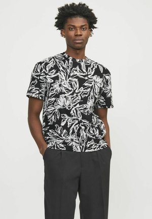 Schwarzes Kurzarm-T-Shirt mit einem weißen Blumenmuster, Rundhalsausschnitt und strukturiertem Stoff, kombiniert mit dunklen Hosen.