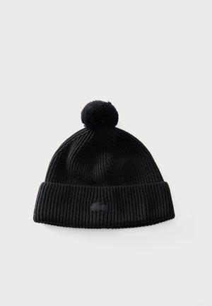 Bonnet en tricot côtelé noir avec un revers plié et un pompon sur le dessus, présenté sur un fond clair.