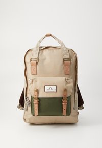 Beige backpack with green front pocket, leather straps, metal hardware, and a tag reading "DOUGHNUT." Includes dual shoulder straps and a top handle.