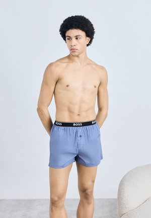 Lichtblauwe boxers met een zwarte elastische tailleband met het "BOSS"-logo. Zachte stof, losse pasvorm en een enkele knoopsluiting aan de voorkant.