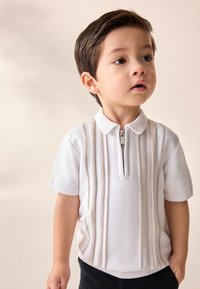 Biela krátky rukáv polokošeľa so zapínaním na zips, s vertikálnymi béžovými pruhmi a textúrovanými detailmi. Kombinovaná s čiernymi nohavicami.