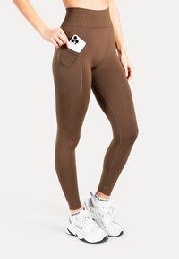 Leggings marroni a vita alta con una tasca laterale per il telefono, caratterizzati da una texture liscia e dettagli di cuciture sottili, abbinati a sneaker bianche.