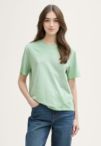 T-shirt en coton vert clair avec un col rond et des manches courtes ; présente un petit logo en relief sur la poitrine et une coupe décontractée.