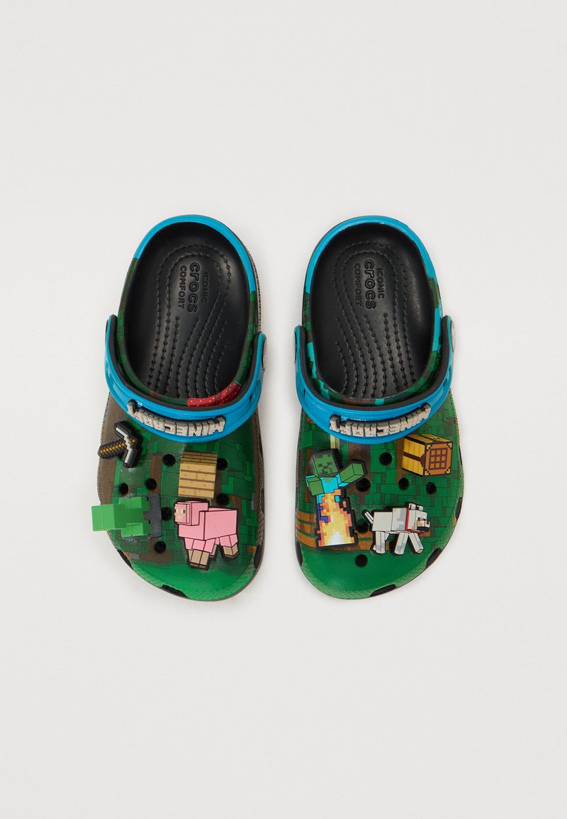 Crocs verdes para niños con correas azules, decorados con charms temáticos de Minecraft que incluyen un cerdo, un perro, una espada y un personaje pixelado.