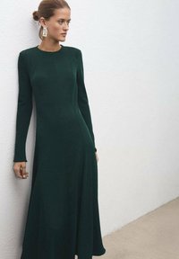 Vestido de manga larga en verde esmeralda con un cuerpo ajustado y falda acampanada. Presenta un tejido texturizado y un escote de cuello redondo.