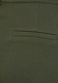 Olijfgroene stof met een gestructureerde afwerking, voorzien van een enkele paspelzak aan de achterkant, die een klassieke, op maat gemaakte ontwerp benadrukt.