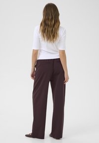Pantaloni a gamba larga in bordeaux scuro, realizzati in tessuto morbido con una superficie liscia. Presentano una tasca posteriore e una silhouette rilassata.