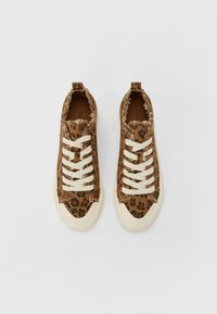 Pruun leopardimustriga kanvas sneakerid, millel on kulunud servad, valged paelad ja kreemjad kummitaldad. Jalatsitel on ka siibriga tõmbeosa kanna peal.