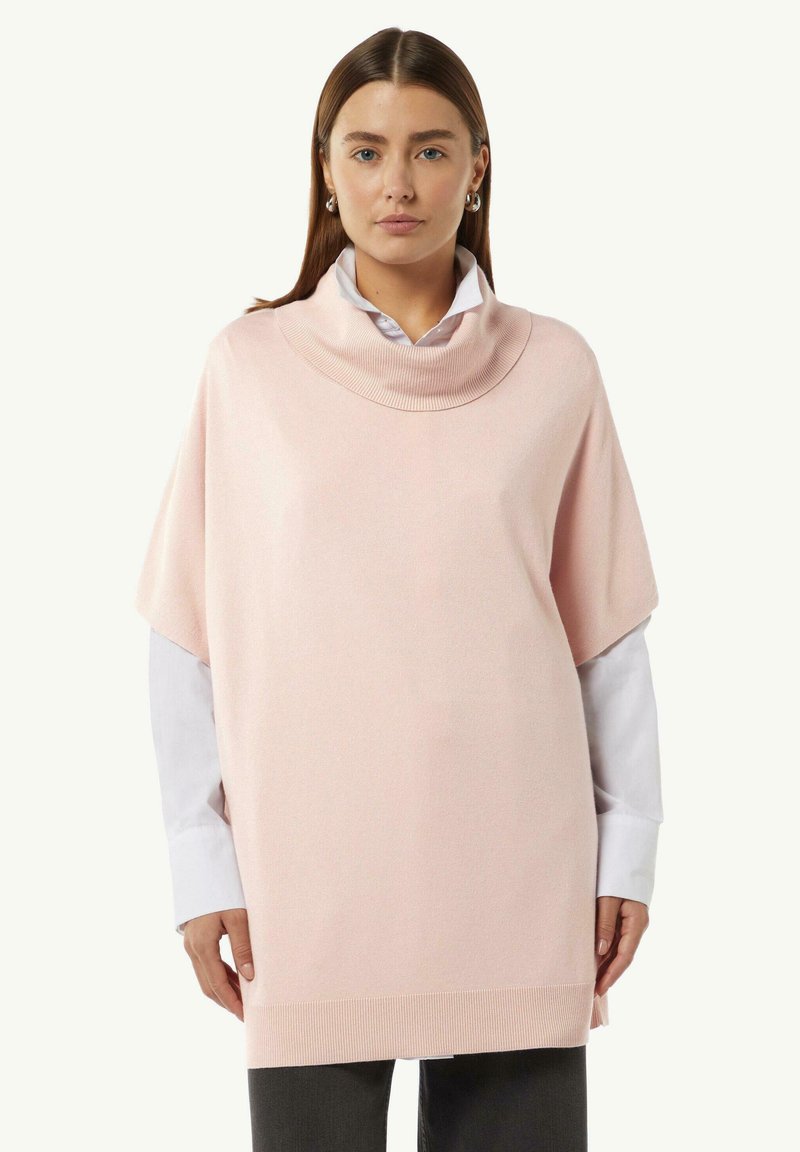 Helles rosa Poncho-Sweatshirt mit einem Ziertausschnitt, kurzen Ärmeln und geripptem Saum. Über einem weißen Hemd mit Kragen getragen, das eine weiche Textur hat.