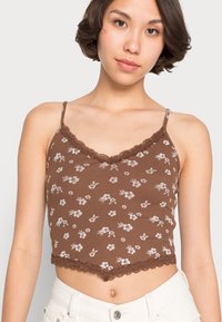 Top cropped castanho com padrão floral branco, acabamento em renda na gola, alças finas ajustáveis e bainha em forma de onda.