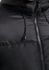 Black puffer jacket with a hood, featuring a full front zipper, drawcord adjusters, and a smooth, shiny finish.
