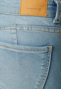 Jeans de mezclilla azul claro con un bolsillo trasero con costuras en contraste y una etiqueta de cuero marrón estampada con "Denim Bershka Est. 98."