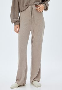 Pantalones de lounge beige claro con canalé, cintura con cordón y corte de pierna amplia. Fabricados con un tejido suave y texturizado que ofrece un silueta relajada.
