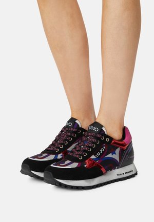 Zapatillas deportivas con un diseño multicolor que incluye ante negro, acentos rojos brillantes y un atrevido logotipo en los cordones y el talón.