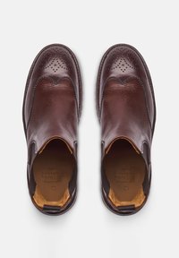 Scarpe slip-on in pelle marrone con dettagli perforati, texture liscia, punta arrotondata, accenti elastici laterali e fodera interna a contrasto.