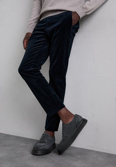 Dark blue corduroy pants with a slim fit, featuring fine ridges, paired with gray suede shoes with a thick rubber sole.