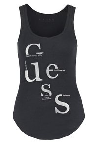 Czarny prążkowany top na ramiączkach z dużymi, błyszczącymi srebrnymi literami piszącymi "Guess" oraz małymi opisowymi słowami rozsianymi wokół liter.