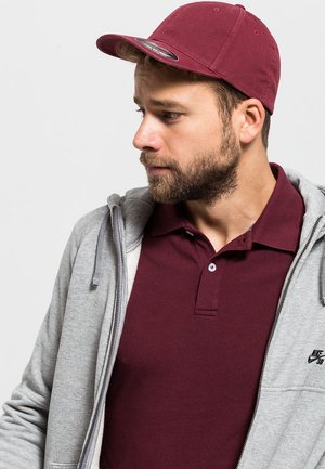 Maroon müts, hall tõmblukuga kapuutsiga sviiter ja maroon polo särk. Sviitril on Nike logo, näidates vabaajarikka kihilise välimuse.