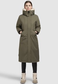 Olivi vihreä pitkä parka, jossa on fleecevuorattu huppu, kaksi sivutaskua ja edessä vetoketju. Materiaali on sileä ja hieman kiiltävä.