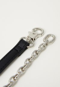 Zwarte leren band bevestigd aan een zilveren metalen sluiting en verbonden met een zilveren ketting met ovale schakels en een kleine zilveren sluiting op een witte achtergrond.